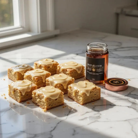 Blondie squares topped with icing beside a jar of maple syrup on a sunlit counter.